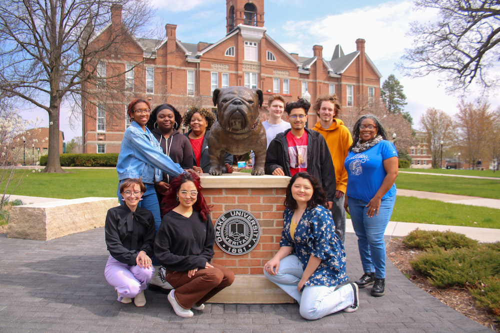 Members of the Bright College Class of 2023 graduating cohort gather for a picture around a bronze statue of Drake's bulldog mascot.