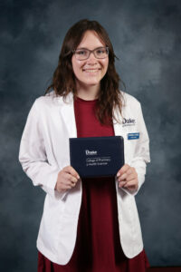 Michaela Schick, a future first-generation pharmacist, posing for a portrait at the 2021 Drake PharmD White Coat Ceremony while wearing a new white coat and holding a padfolio with the Oath of a Pharmacist printed inside.