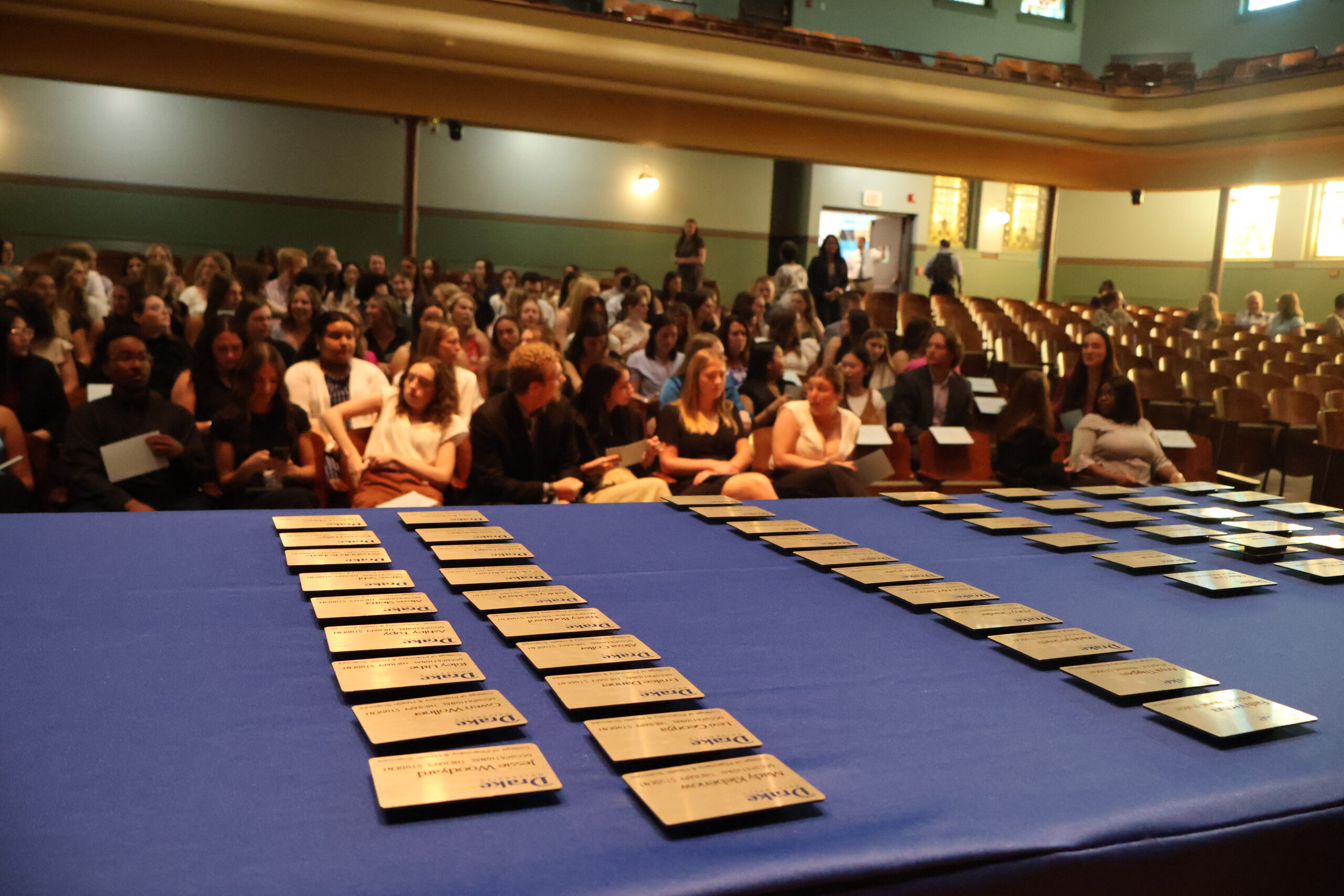 name badges laying out on table at CPHS pinning ceremony, with student recipients sitting in the audience in the background