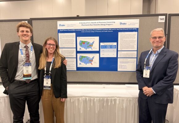 two drake pharmacy students and their faculty mentor stand next to their research poster at the conference