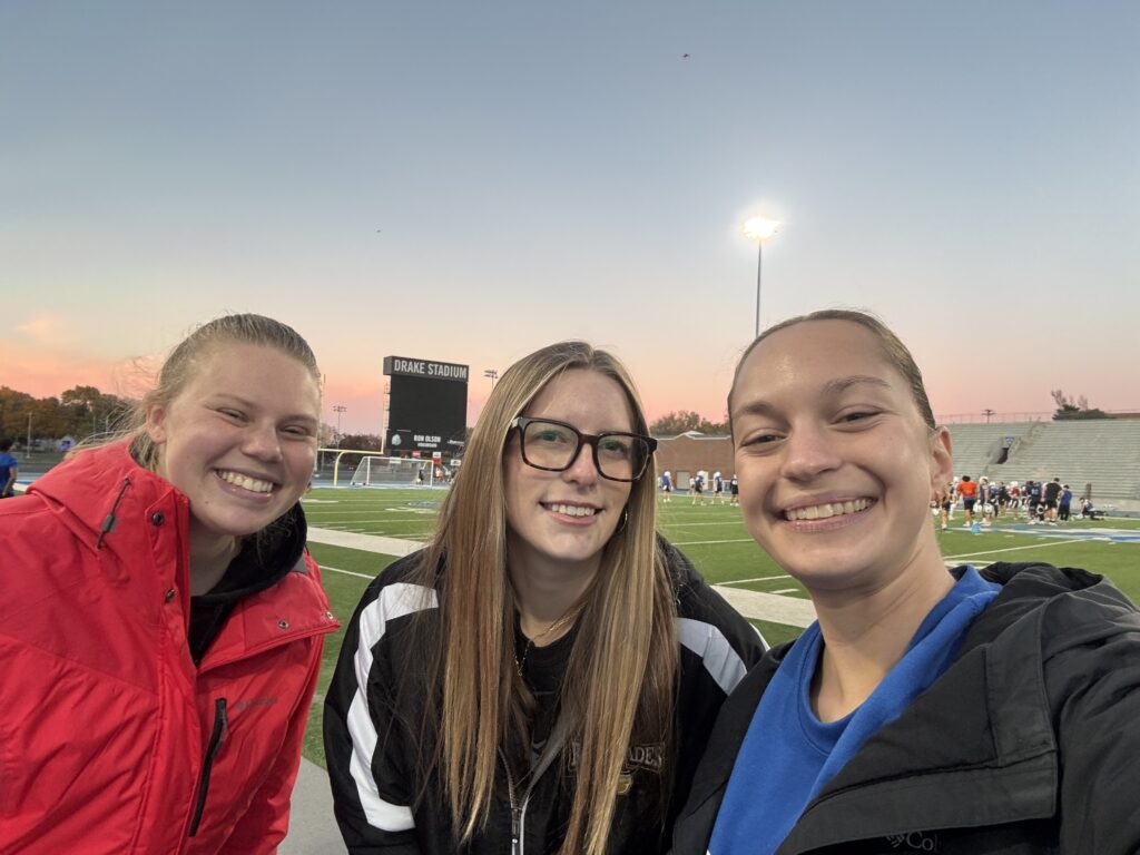 Isabella Ansani smiling with athletic trainers on Drake football field