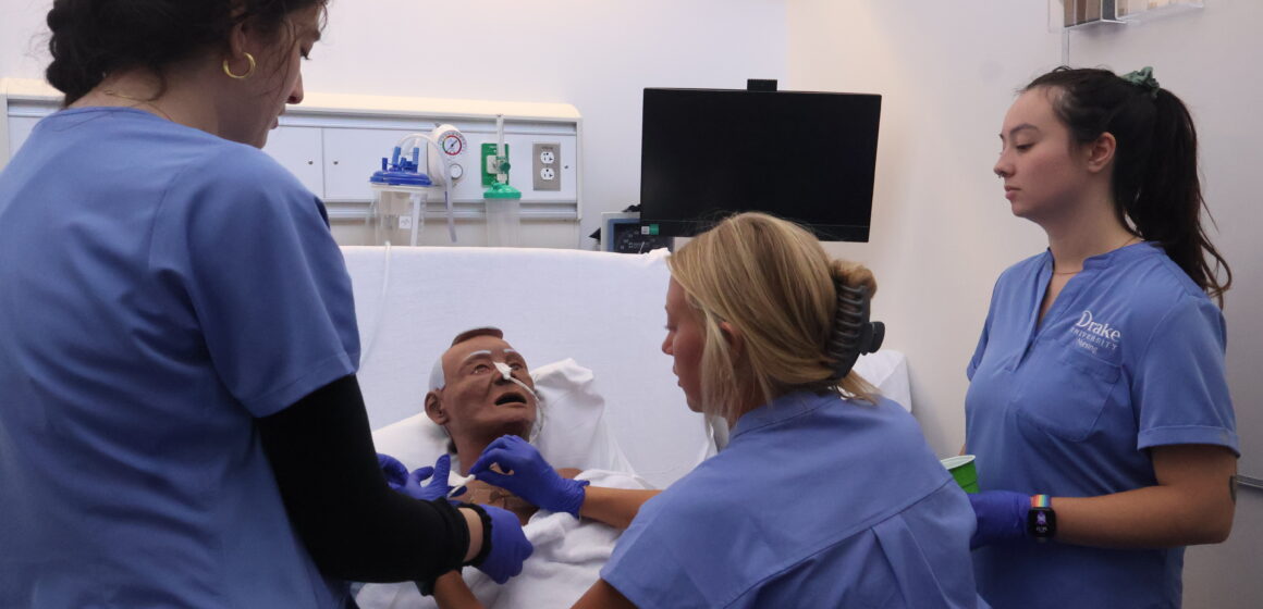 IMG_6003 Nursing students gather around a mannekin to adjust tubing attached to his face