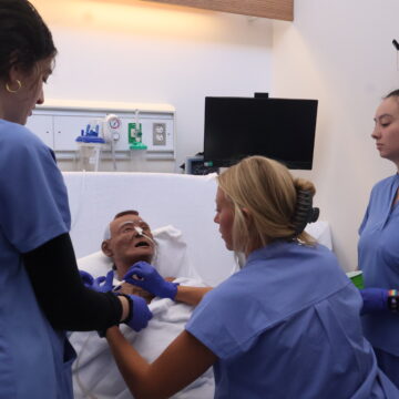 Nursing students gather around a mannekin to adjust tubing attached to his face