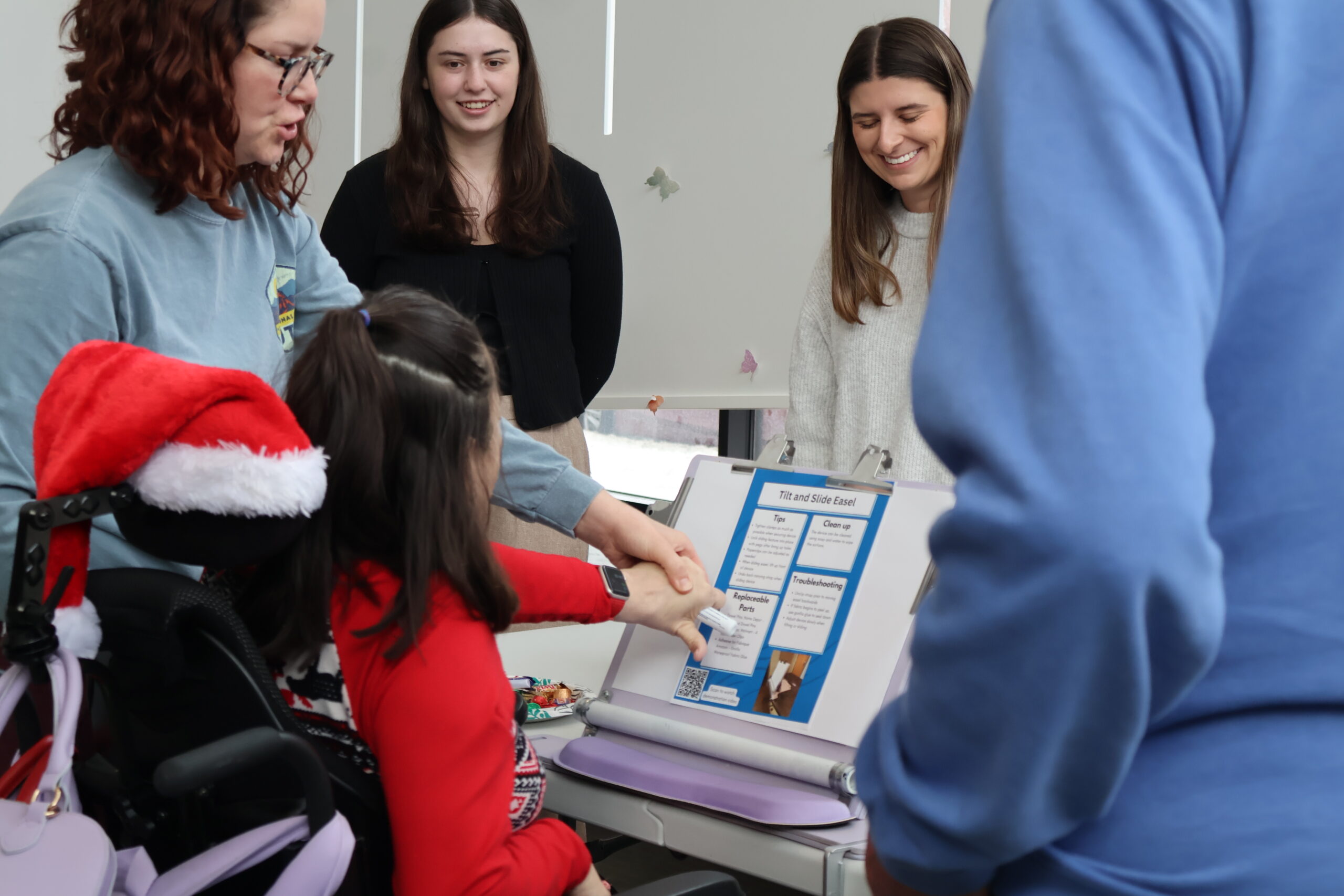 Students smile as a client's caregiver guides her hand to demonstrate the easel