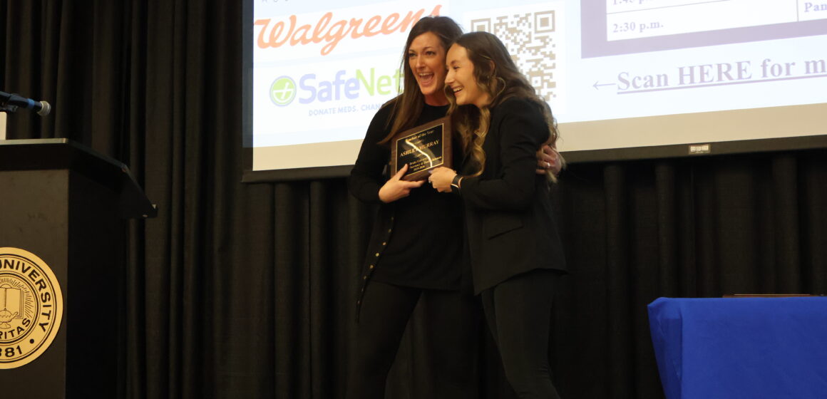 A Drake faculty member and student hug and smile, both holding an award plaque