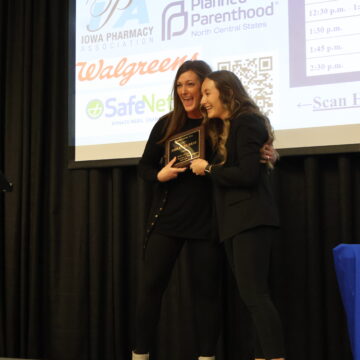 A Drake faculty member and student hug and smile, both holding an award plaque