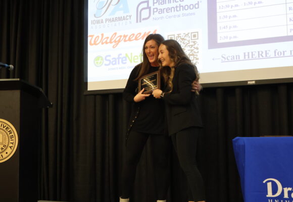 A Drake faculty member and student hug and smile, both holding an award plaque