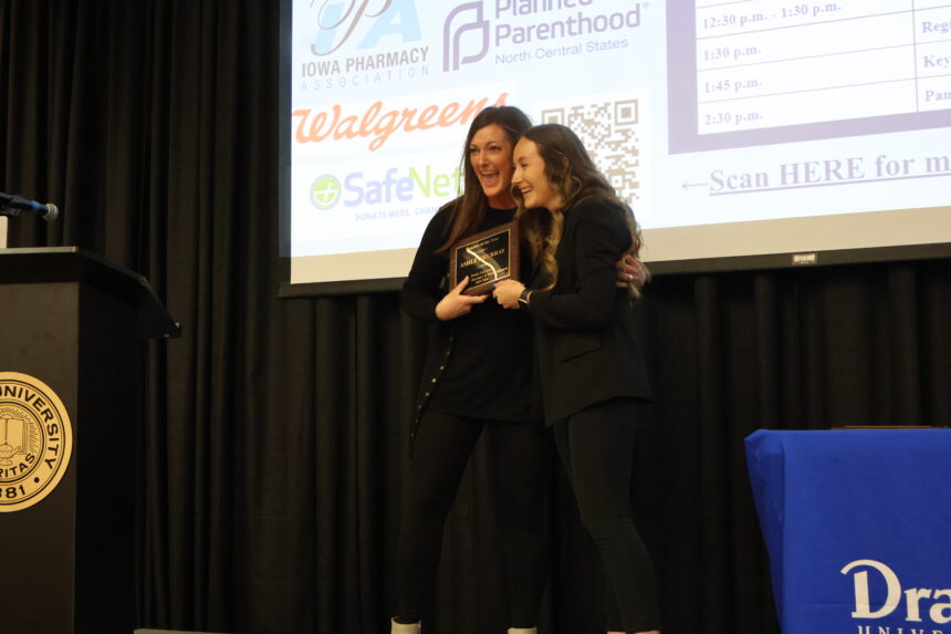 A Drake faculty member and student hug and smile, both holding an award plaque