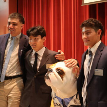 Three Drake students wear their pins and pose with a bulldog statue