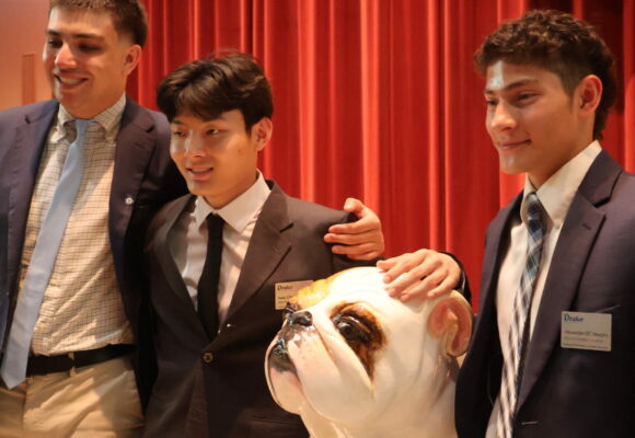 Three Drake students wear their pins and pose with a bulldog statue